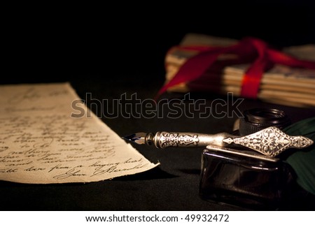 Love letter, antique quill and black ink and stack of letters tied with a red ribbon.