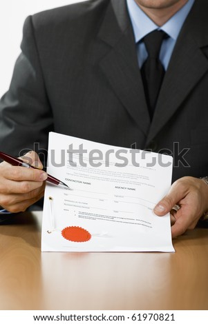 Bussinessman (or notary public) holding pen pointing at signature place on a contract document