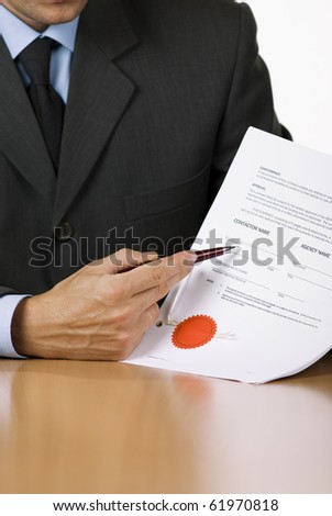 Bussinessman (or notary public) holding pen pointing at signature place on a contract document