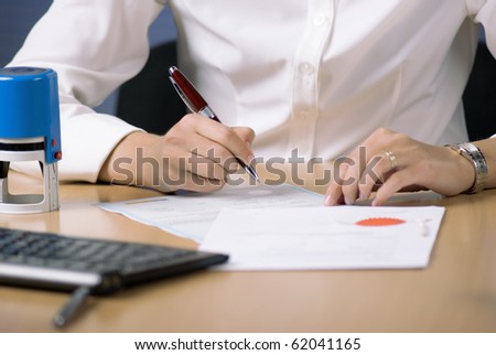 Young businesswoman (or notary public) sitting at the desk in office and signing document