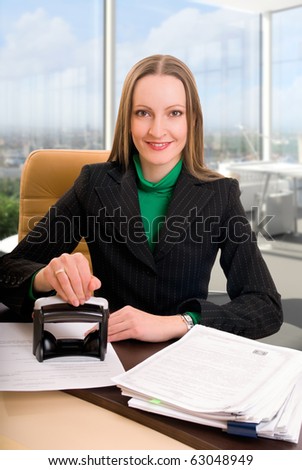 Young businesswoman (or notary public) seating at the desk in office and stamping document
