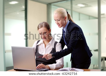 Two contemporary business women in an office discussing work on laptop
