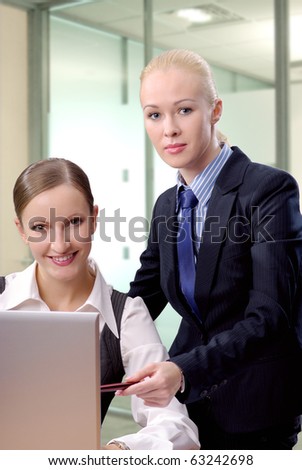 Two contemporary business women in an office discussing work on laptop looking on camera