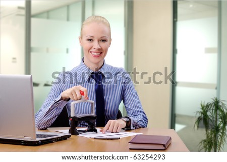 Young businesswoman (or notary public) sitting at the desk in office and stamping document looking at camera