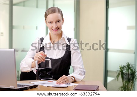 Young businesswoman (or notary public) sitting at the desk in office and stamping document