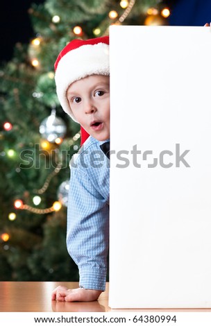 4 years old boy holding blank near New Year\'s tree with expression on his face