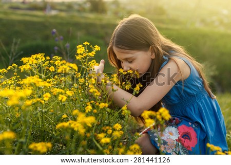 Little girl enjoys the smell of flowers in the meadow