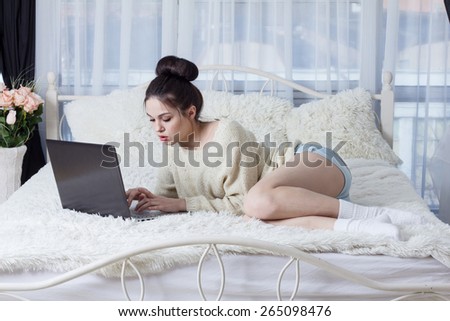 Brunette lying on the bed and that someone typing on a laptop