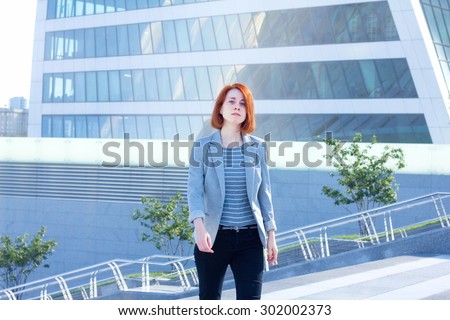Redhead business woman up the stairs on the background of a skyscraper