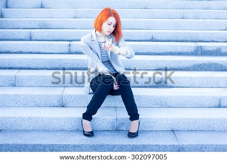Redhead attractive woman sitting outside on the stairs and watching time