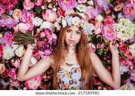 A beautiful young girl with flowers bouquet near a floral wall.