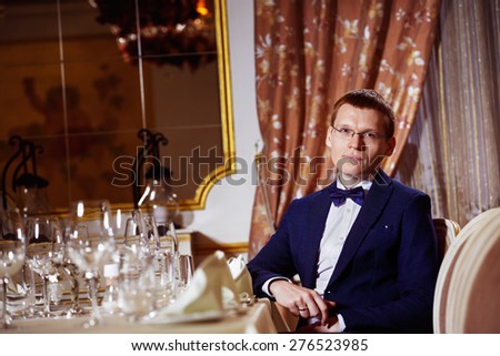 Elegant dressed businessman in glasses is sitting in luxury restaurant waiting for dinner.