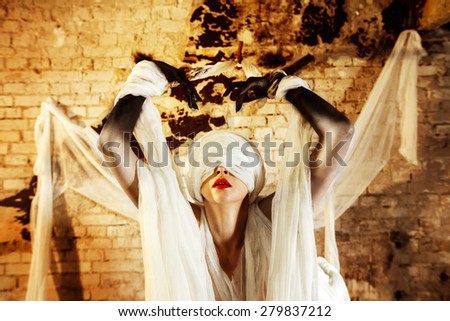 Closeup portrait of a woman with closed by bandage face and red lips stretching hands up at bricks wall background.
