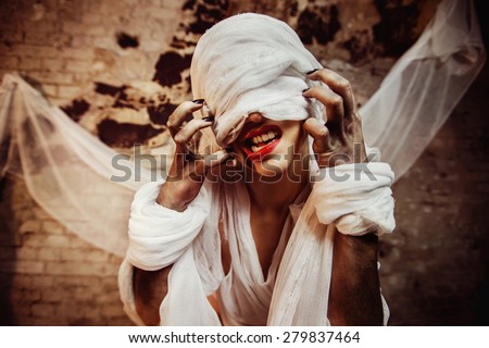 Closeup portrait of insane creature scratching her closed by bandage drawn face and red lips at bricks wall background.