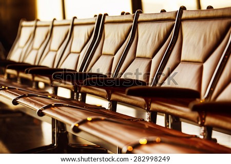 Row of leather chairs in international airport terminal at window background with yellow sunlight.