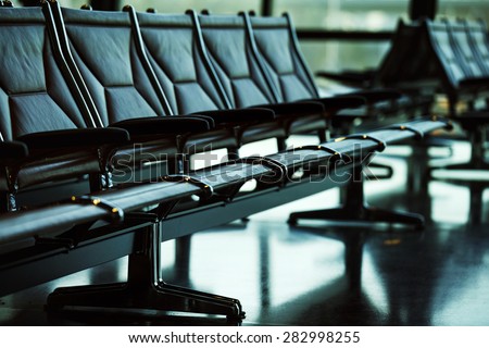 Row of leather chairs in international airport terminal at window background.