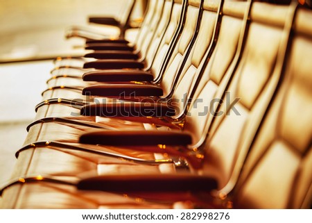Row of leather chairs in international airport terminal at window background with yellow sunlight.