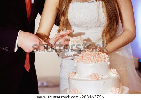 Closeup image of wedding couple cutting beautiful holiday cake with roses.