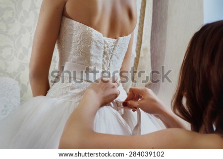 A closeup image of wedding preparations. Bridesmaid is helping put bride elegant luxury dress.