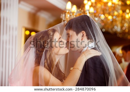 Closeup portrait  of beautiful wedding couple covered in veil kissing at indoors mirror background. Concept of love and family.