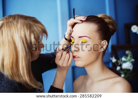 Professional makeup process. Artist is making face style of a young beautiful model at  blue studio background.