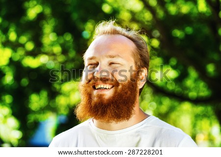 Closeup portrait of happy mature man with red beard and mustache is laughing at summer green park background.