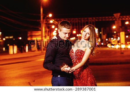 Closeup portrait of beautiful young couple embracing at night city street at colorful lights background.