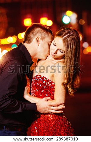 Closeup portrait of beautiful young couple kissing at night city street at colorful lights background.