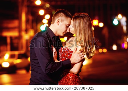 Closeup portrait of beautiful young couple kissing at night city street at colorful lights background.