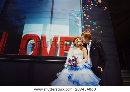Happy wedding couple is laughing at street shop window with caption Love background.