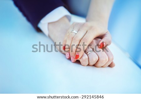 Closeup image of man and woman hands with wedding ring holding tenderly at blue background.