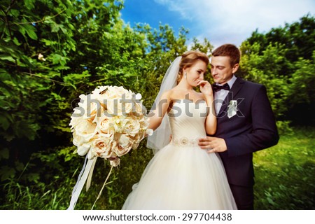 Closeup image of white roses wedding bouquet and laughing bride and groom at summer park background. Focal point on bouquet.