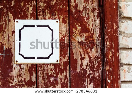 Closeup image of red wooden rusty door with white blank plate at bricks background.