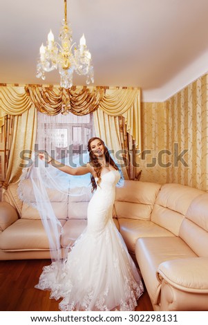 Beautiful young bride in white dress is standing and holding her veil.
