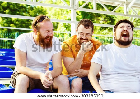 Three young cheerful friends are talking and laughing at summer day stadium background.