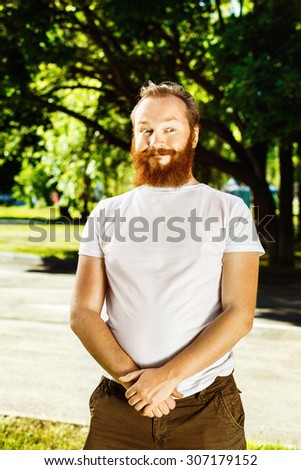 portrait of funny red hair bearded man with curious face, funny look at green summer outdoors park background.