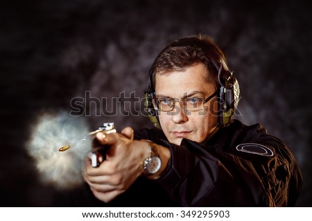 Closeup portrait of man with gun making shot at training club at dark background.