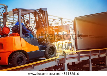 Forklift is putting cargo from warehouse to truck outdoors at sunny sky background.
