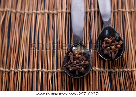 Two wooden spoons full of cloves on a wooden background