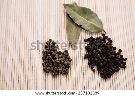 A pile of green peppercorns, a pile of black peppercorns and bay leaves