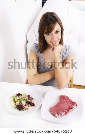 young woman eating salad and meat, smiling and looking in camera