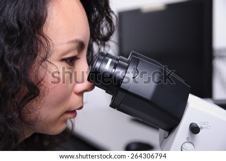 Female chinese scientist looking into microscope eyepieces