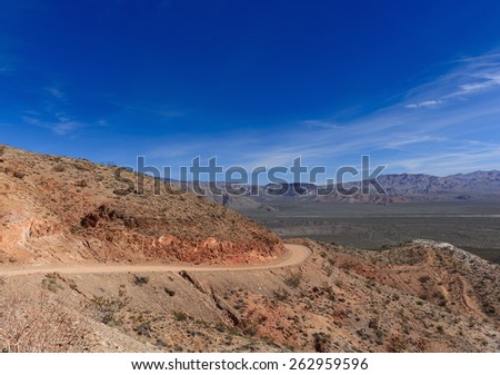 Curve on unpaved Death Valley road with red land, blue sky and mountains on background