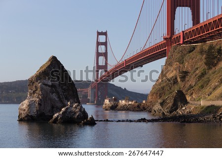 Horizontal image of big sea rocks near Golden Gate bridge with old lighthouse and fog station under the bridge in soft morning light. San Francisco. California. USA
