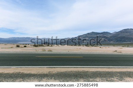 Horizontal paved road in desert with striped mountains on background