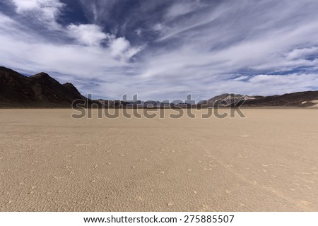 Dry lake bed in Mojave desert with cracked mud on a lake floor, blue sky, clouds and mountains. Racetrack Playa. Death Valley national park. California. USA.