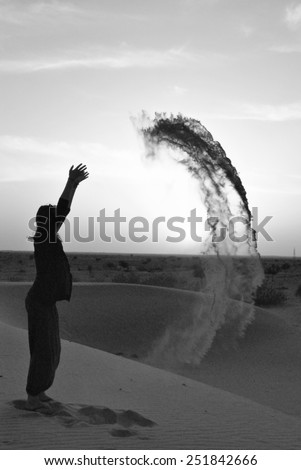 A woman throwing sand in a desert sunset in black and white.