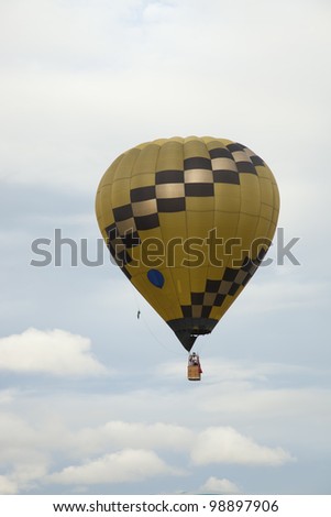 Yellow and Black Balloon Yellow hot air balloon gliding easily with cloudy blue sky in the background.