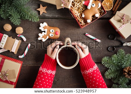 Woman holding in hands hot christmas tea with candy cane against decorations, gift boxes, ribbon and ginger bread on wooden board. Xmas concept. Eye bird view.