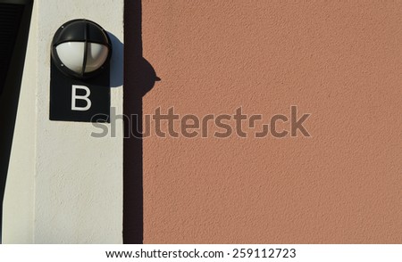Pastel colors in a residential building entrance. Outdoor lamp with letter B in a building. Pastel colored wall. Subtle colors in housing exterior. Different color layers in a house.